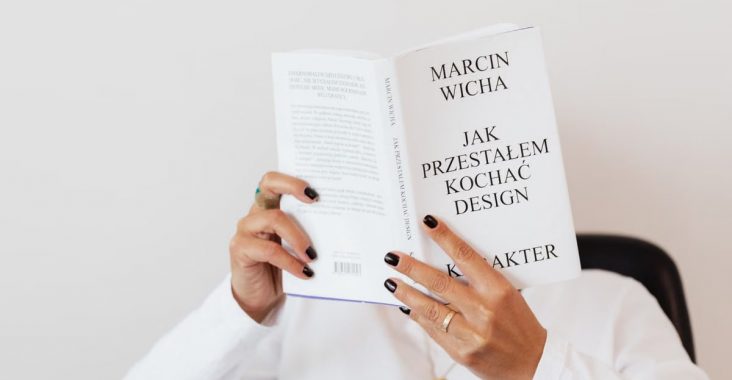 Anonymous female in white shirt with gold chain on neck reading interesting book covering face while sitting on black chair
